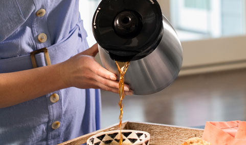 Woman touching exterior of the cool-touch thermal carafe.